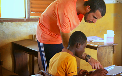 Male volunteer leans over and helps child with school work