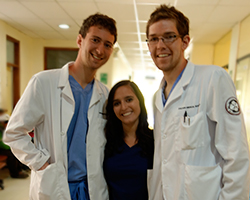 Three medical students in white lab coats smile for the camera.