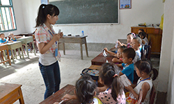 Female volunteer stands in front of children and teaches at school in China