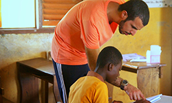Male volunteer leans over and helps a child with homework