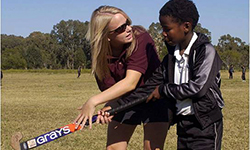 Female volunteer teaches young south african boy how to hold a hockey stick