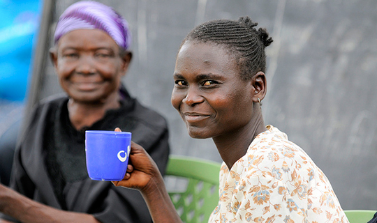 Kenyan woman holds a cup of tea and smiles at the camera
