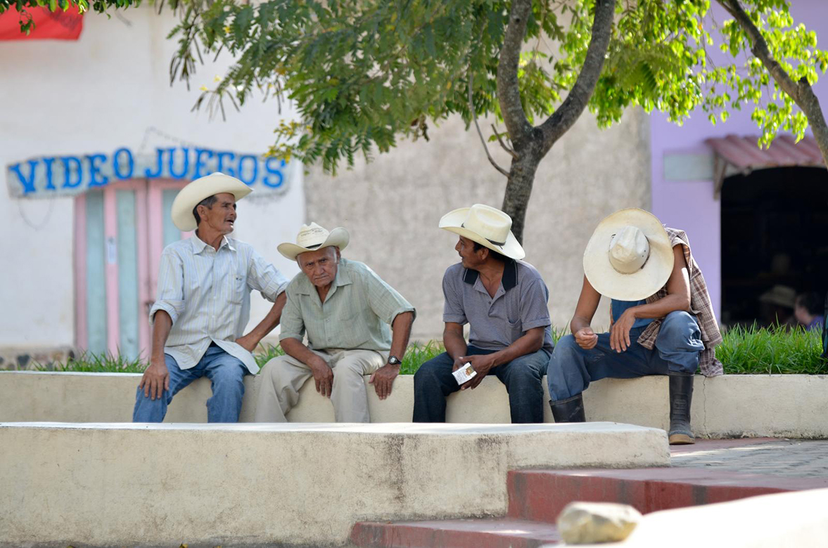 Four Honduran farmers wearing cowboy hats sitting on a bench talking