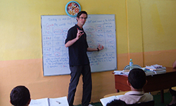 Male volunteer stands in front of white board and teaches classroom of children