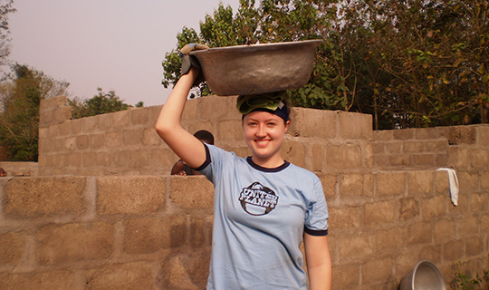 Girl wearing United Planet tshirt holds bowl ontop of her head in Ghana